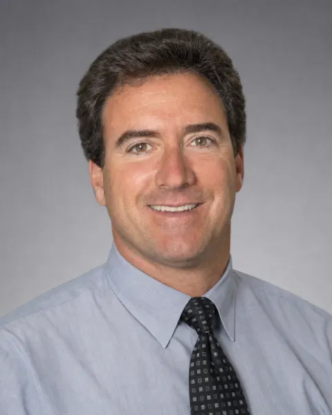 Mark Schraeder, Executive Director, smiling, in a light blue shirt and a dark patterned tie