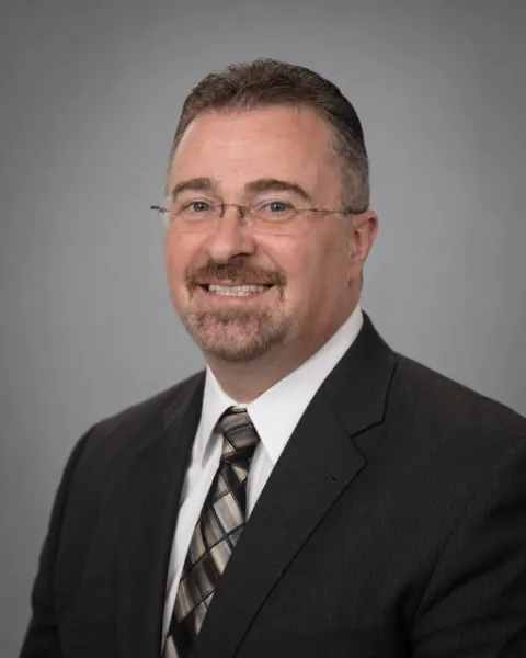 Michael Klijian, attorney, in rimless glasses, a dark pinstripe suit and a patterned tie, smiling