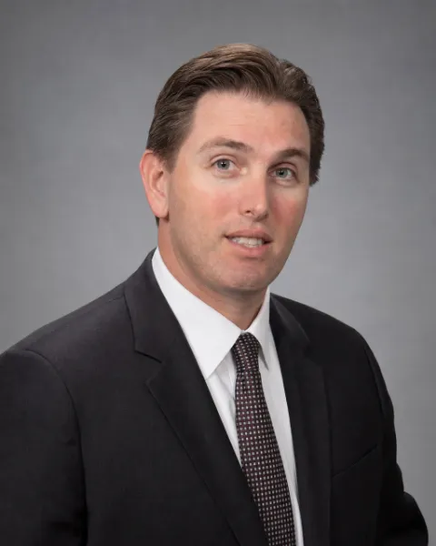 Scott Desind, attorney, with swept-back brown hair, in a dark suit, white shirt and dark tie